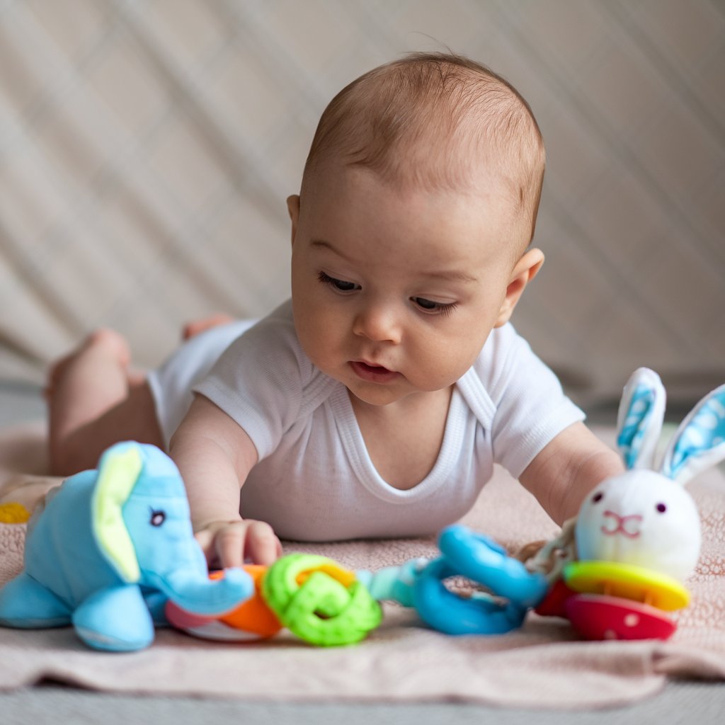 An overhead view of a baby on their tummy during tummy time, with colorful toys placed in front of them. The image captures the baby reaching for the toys, showing engagement and exploration. The play area is set up with a soft blanket and gentle patterns to create a safe space for play.